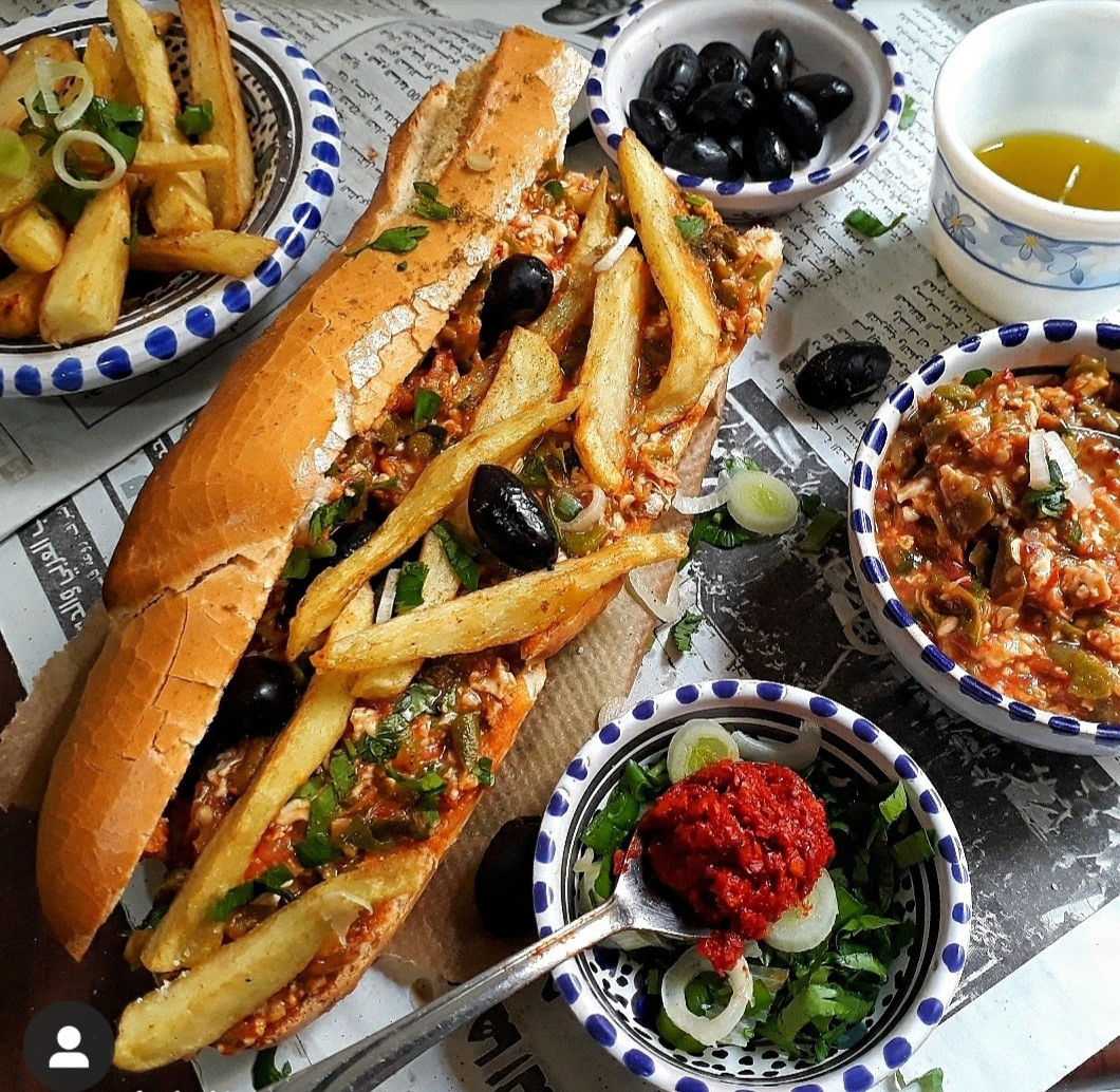 kafteji sandwich with fries and harissa on table with other condiments